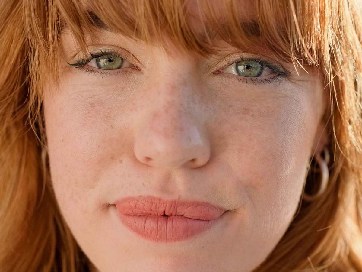 Nahaufnahme einer jungen Frau mit rotblonden Haaren und hellen Augen, die zur&uuml;ckhaltend l&auml;chelt.