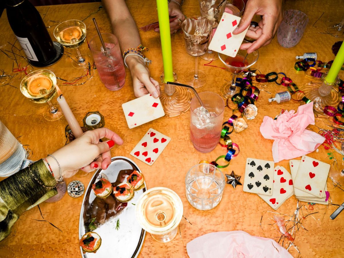 Tisch mit Gl&auml;sern, festlicher Deko und H&auml;nden mit Spielkarten