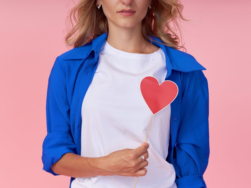 Frau mit blauer Bluse hält ein Herz aus Papier vor sich