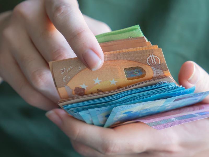 Eine Hand zählt einen dicken Stapel Euro-Geldscheine in verschiedenen Farben, mit Fokus auf einen 50-Euro-Schein.