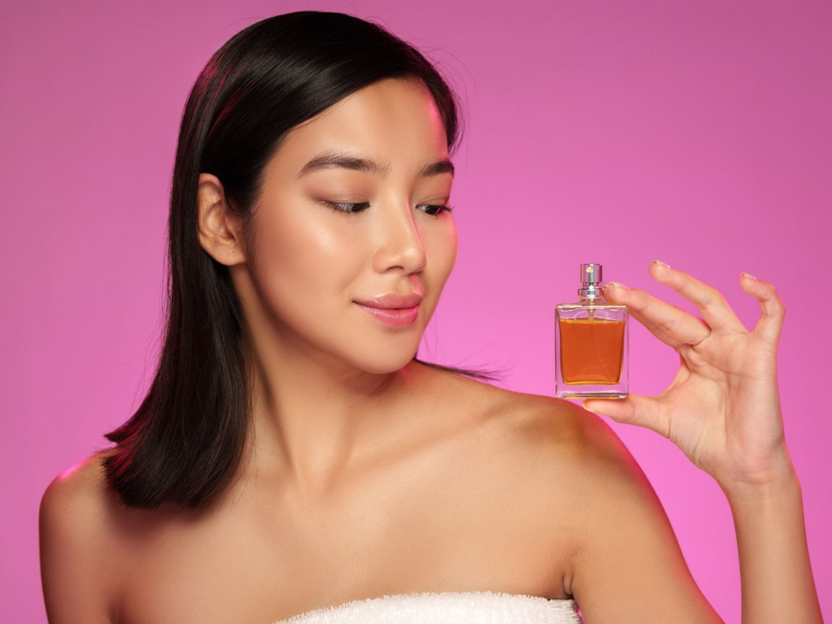 Frau vor pinkem Hintergrund, die ein Parfum in der Hand h&auml;lt