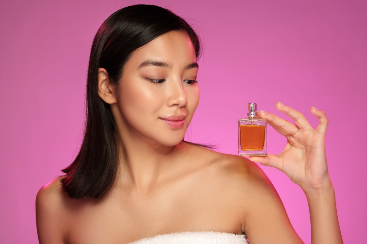 Frau vor pinkem Hintergrund, die ein Parfum in der Hand hält