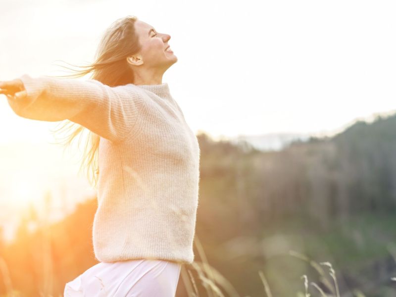 Frau auf einem Feld und ausgestreckten Armen lächelt