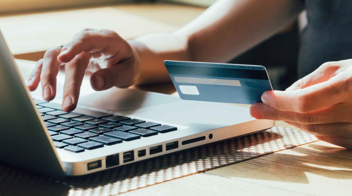 Frau tippt mit einer Hand auf dem Laptop und hält in der anderen Hand ihre Bankkarte.