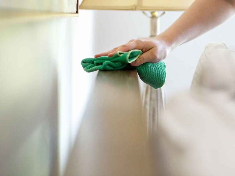 Frau wischt im Schlafzimmer Staub.