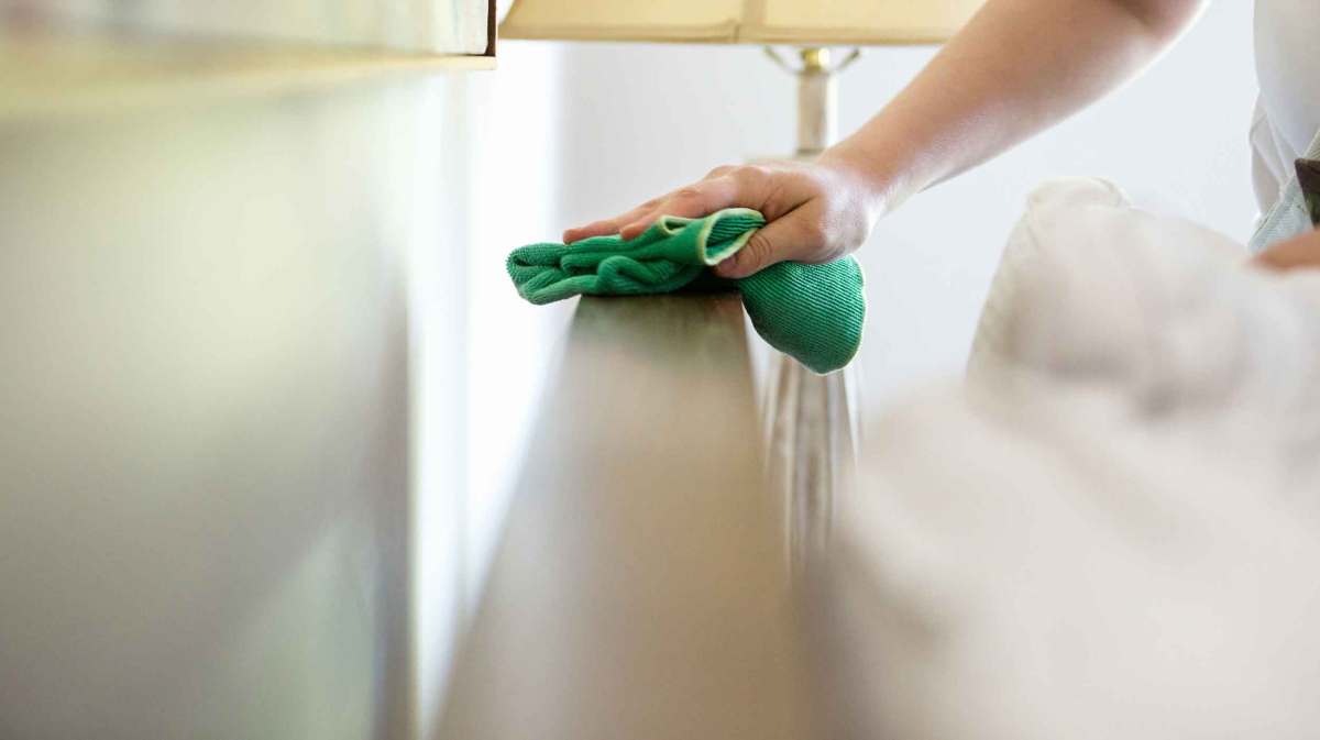 Frau wischt im Schlafzimmer Staub.