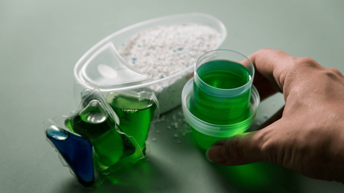 Person stellt Waschpulver, Flüssigwaschmittel & Wäsche-Pods auf eine Ablage