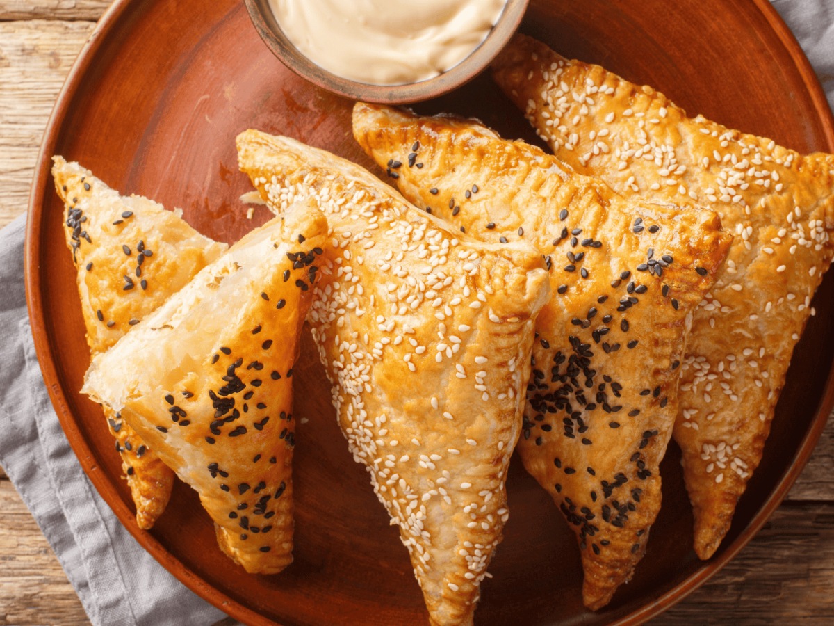 Bl&auml;tterteigtaschen mit Sesam auf einem roten Teller.