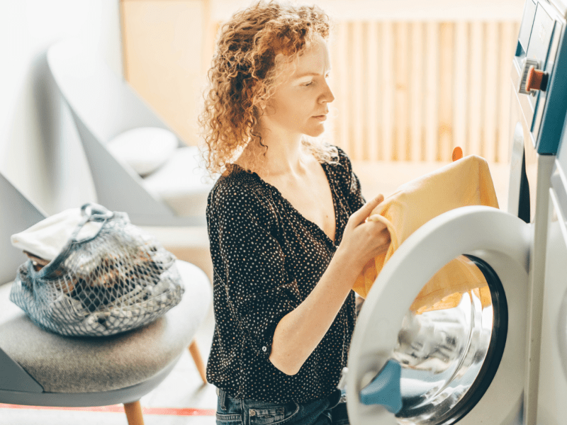 Frau in der Waschküche in der Nähe der Waschmaschine mit schmutziger Kleidung