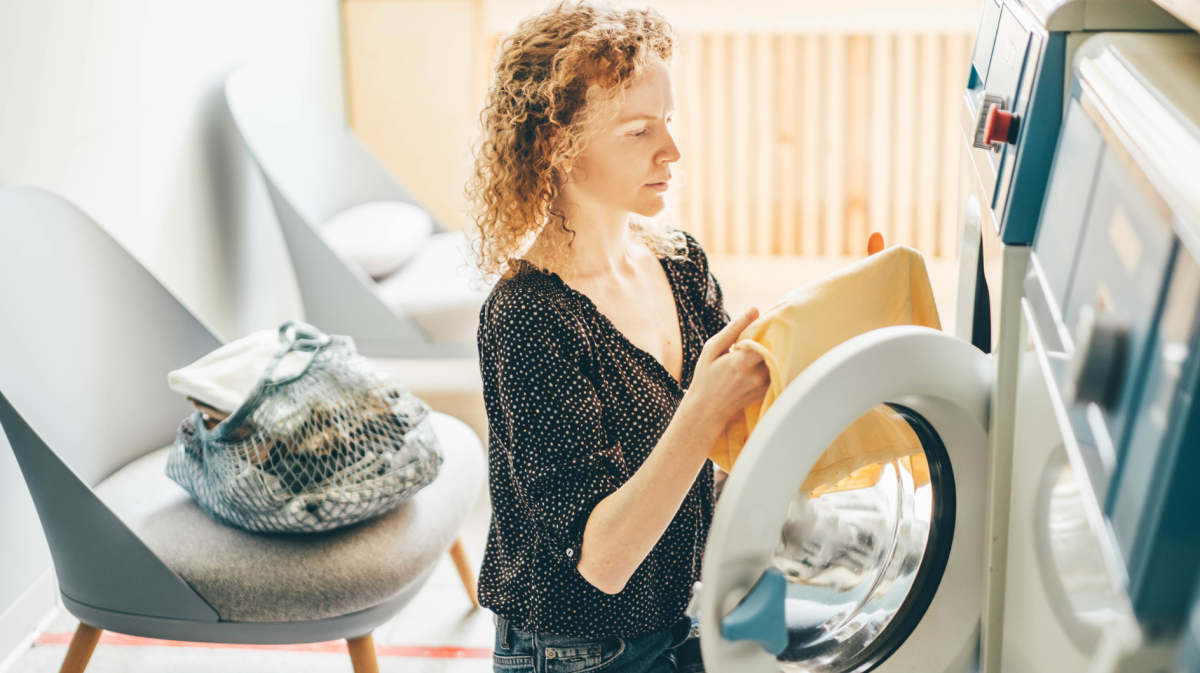 Frau in der Waschküche in der Nähe der Waschmaschine mit schmutziger Kleidung