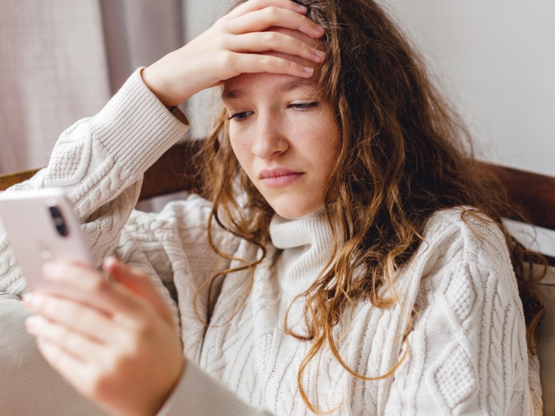 Junge Frau schaut nachdenklich auf ihr Handy.