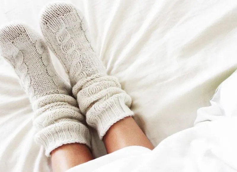 Füße in gestrickten Wollsocken auf Bett
