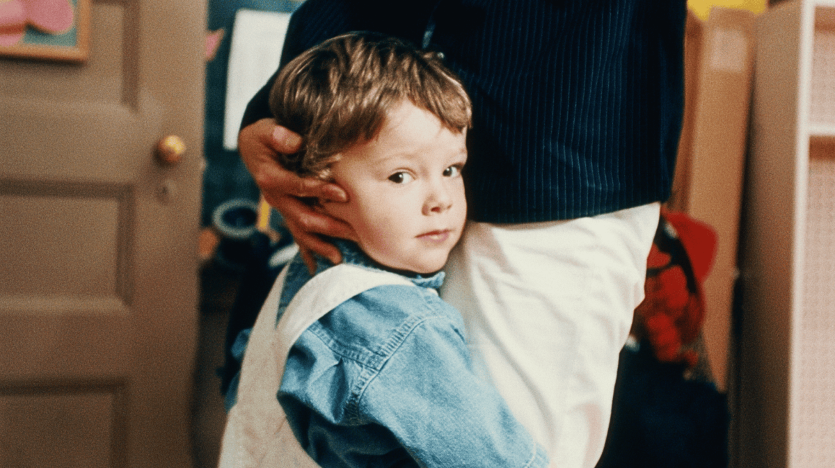Kind umarmt die Beine einer Frau bei der Verabschiedung in der Kita.