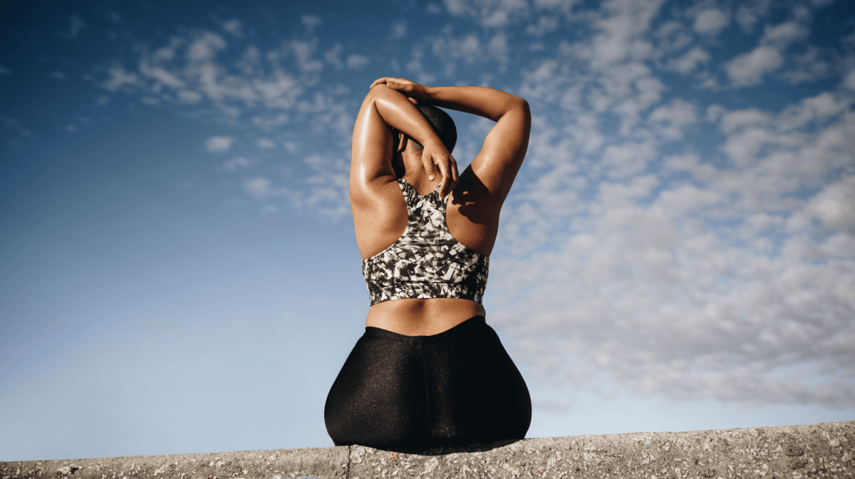 Plus size Frau sitzt auf einer Mauer und streched die Arme