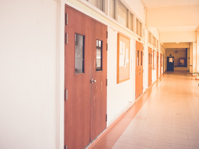 Bild eines leeren Schulflurs mit Sonnenlicht, das durch die Fenster auf der rechten Seite leicht hineinscheint.