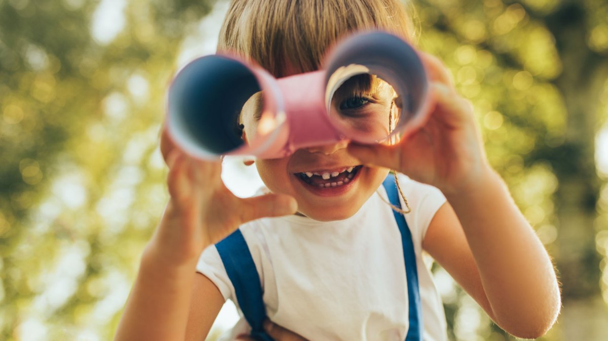 Nahaufnahme eines Kindes, das sich aus Toilettenpapierrollen ein Fernrohr gebaut hat und hindurchschaut.