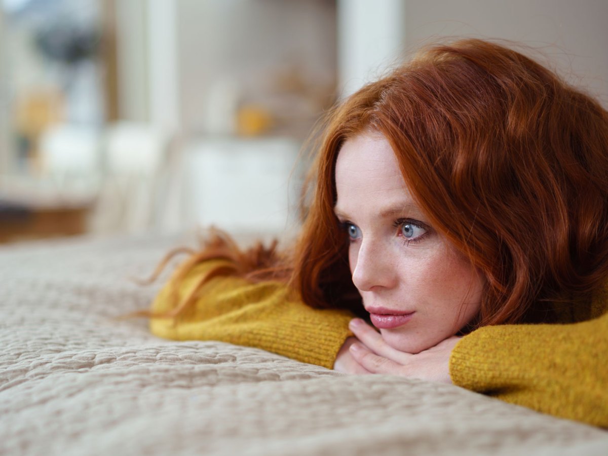 Frau mit roten Haaren liegt auf dem Bett und blickt ernst