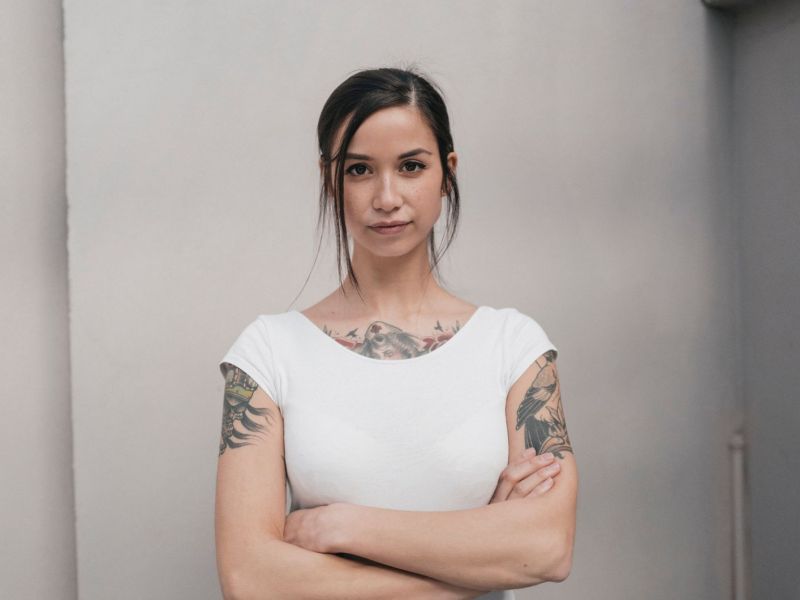 Frau mit Tattoos, verschränkten Armen und weißem Shirt ist stur.,