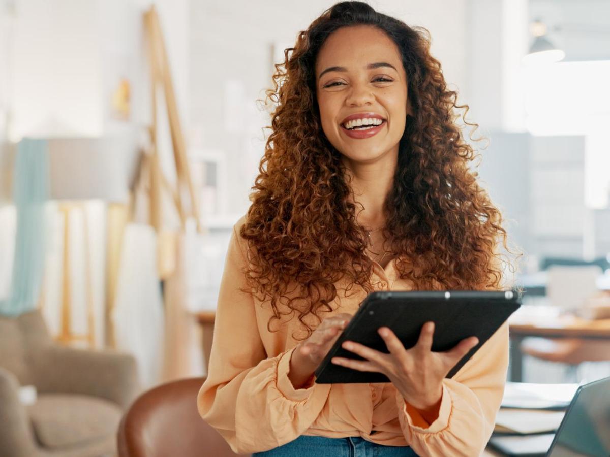 Frau mit Tablet steht im B&uuml;ro und lacht.