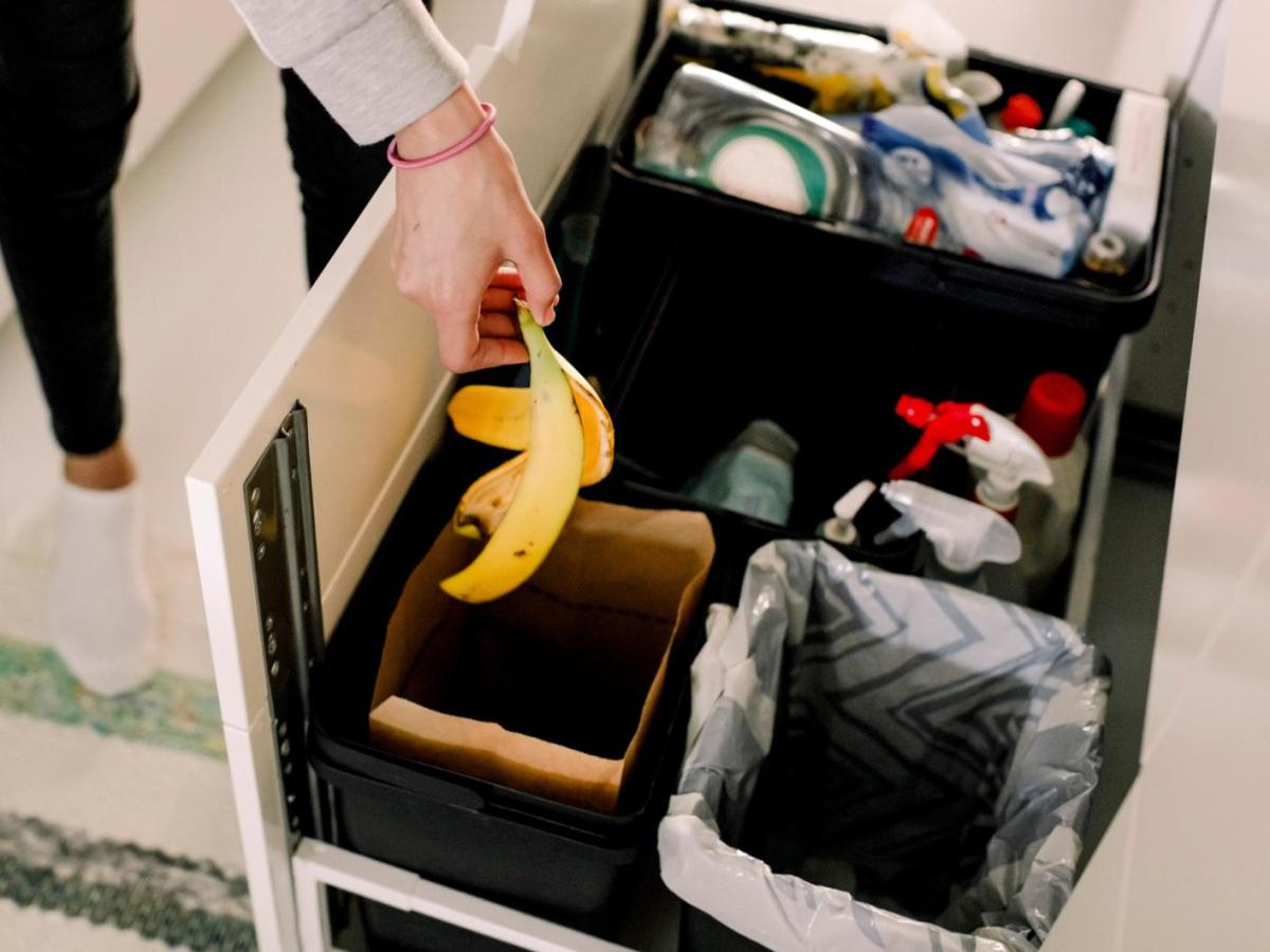 Frau wirft eine Bananenschale in einen M&uuml;lleimer in der K&uuml;che.