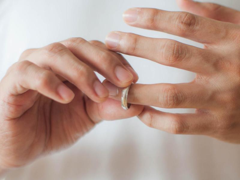 Frau mit weißem Shirt zieht sich den goldenen Ehering vom Finger.