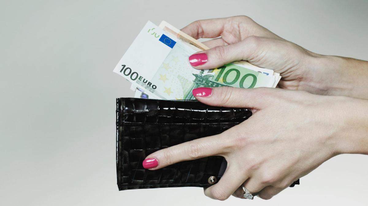 Frau legt Geldscheine in ein dunkles Portemonnaie.