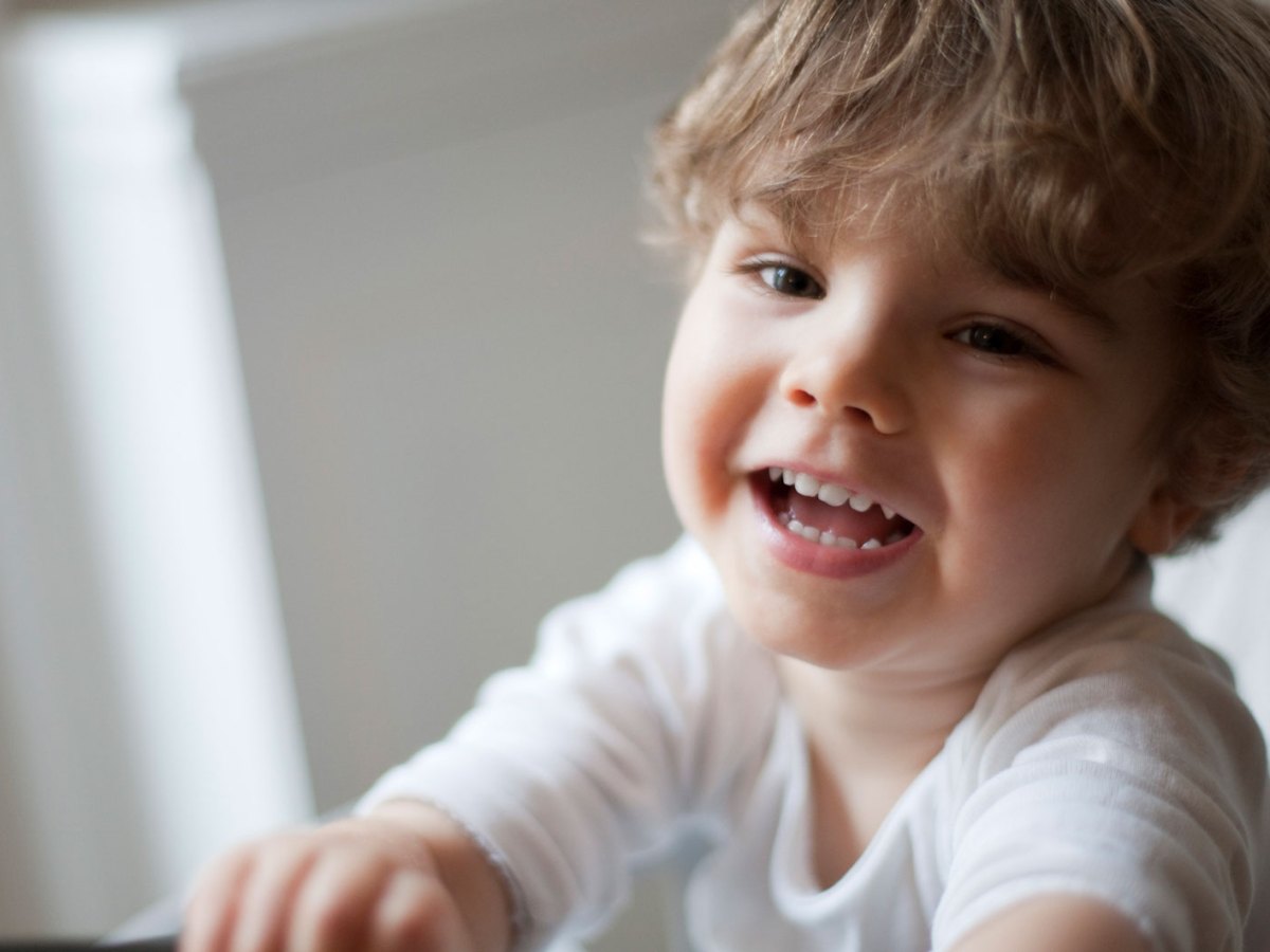 Nahaufnahme eines Dreij&auml;hrigen im Stuhl, der an der Kamera vorbei lacht.