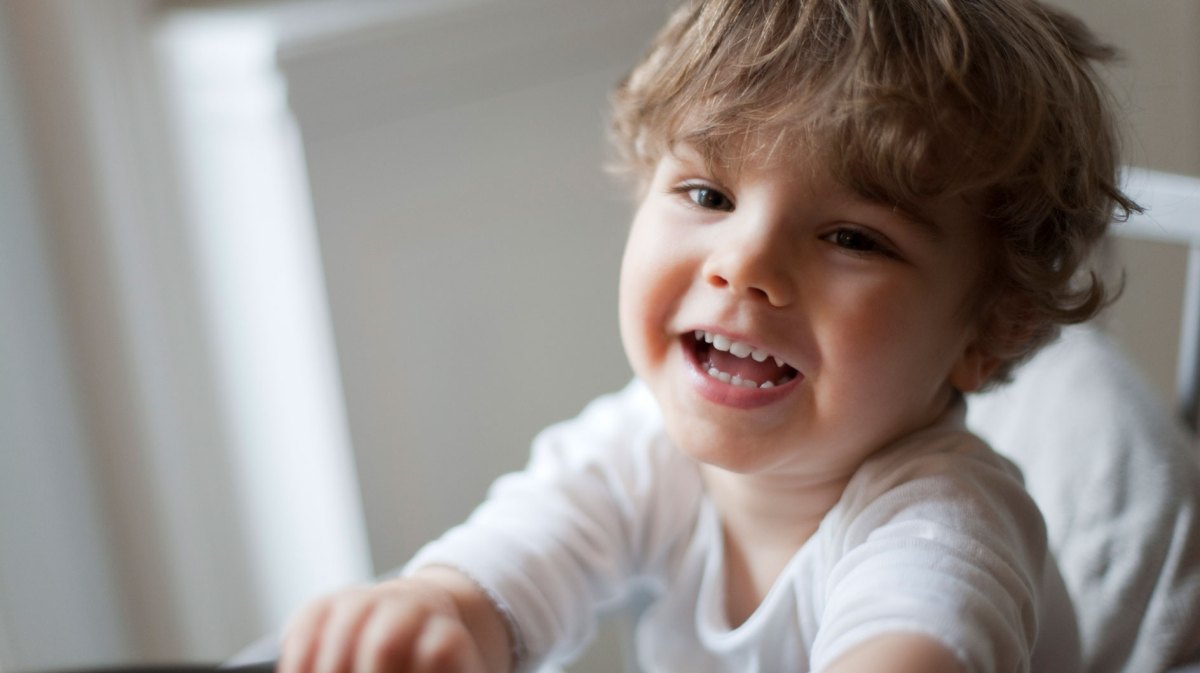 Nahaufnahme eines Dreijährigen im Stuhl, der an der Kamera vorbei lacht.