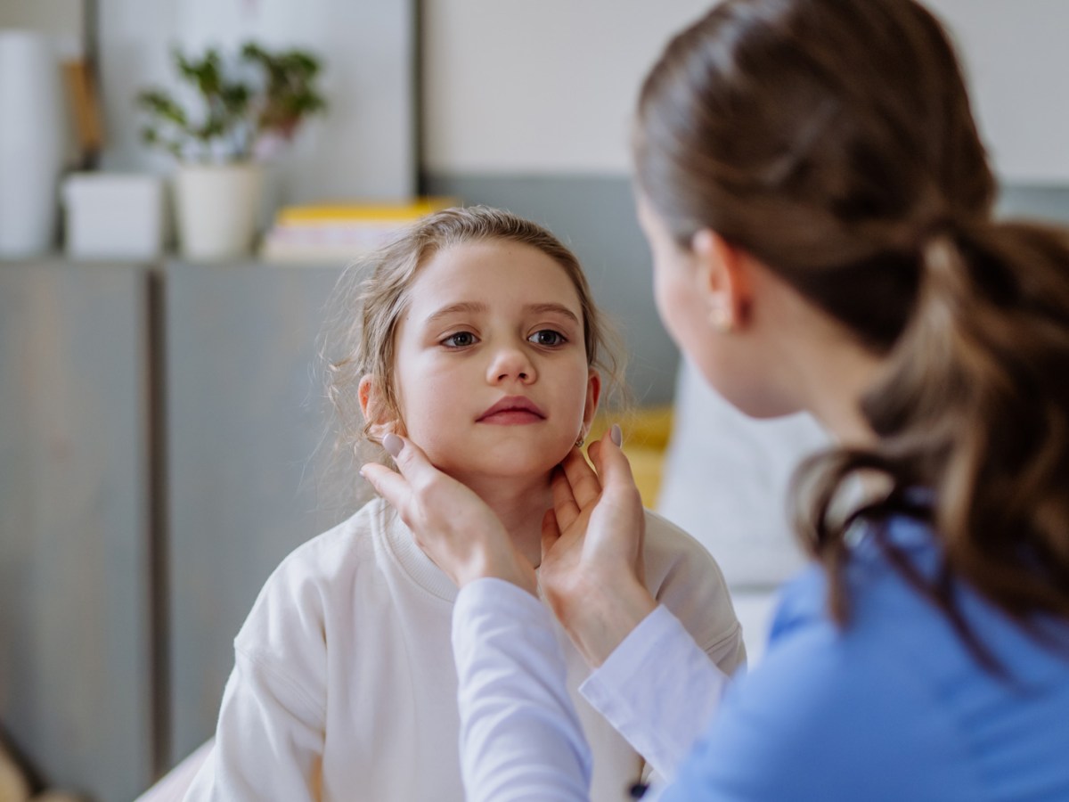 Junge Ärztin untersucht den Hals mittels Tastuntersuchung eines Mädchens, ca. 6 Jahre alt.