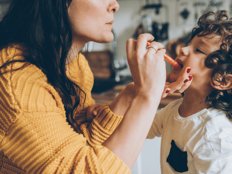 Mutter mit braunen Haaren gibt ihrem kleinen Sohn Medizin in einer Pipette.