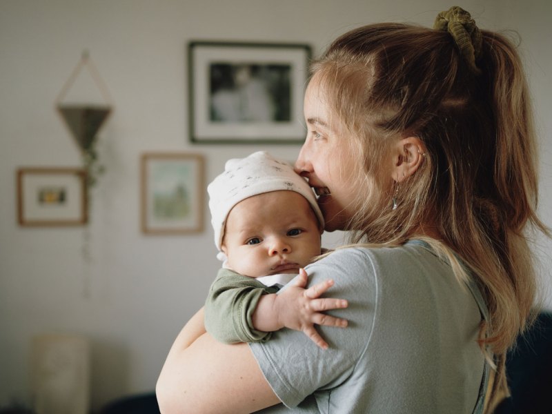 Mutter hält kleines Baby im Arm und schaut aus dem Fenster.