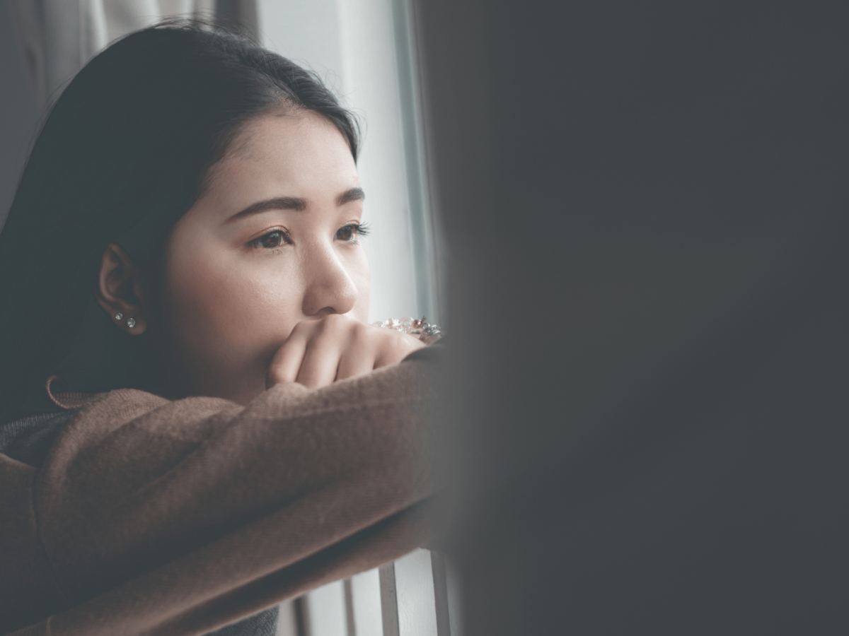 Frau schaut nachdenklich aus dem Fenster