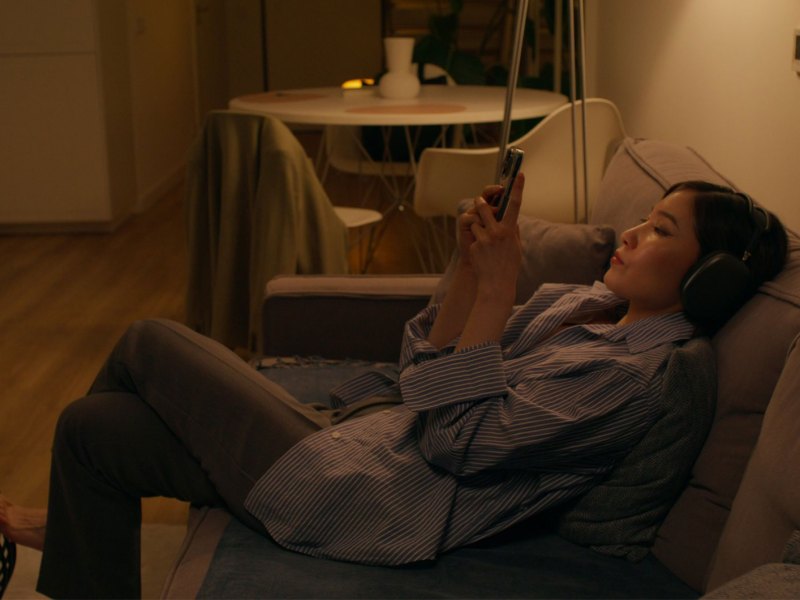 Frau sitzt im Halbdunkel auf der Couch und scrollt durchs Handy.