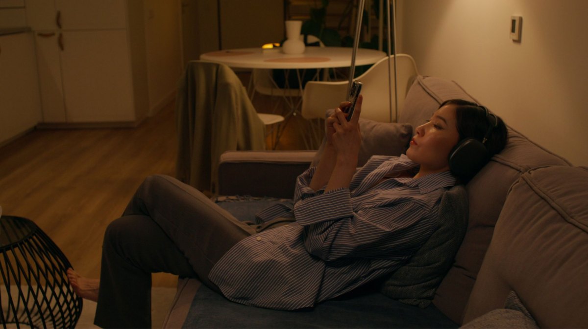 Frau sitzt im Halbdunkel auf der Couch und scrollt durchs Handy.