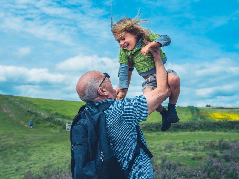 Großvater und Enkel auf einer Wanderung. Der Großvater hebt seinen Enkelsohn in die Luft.
