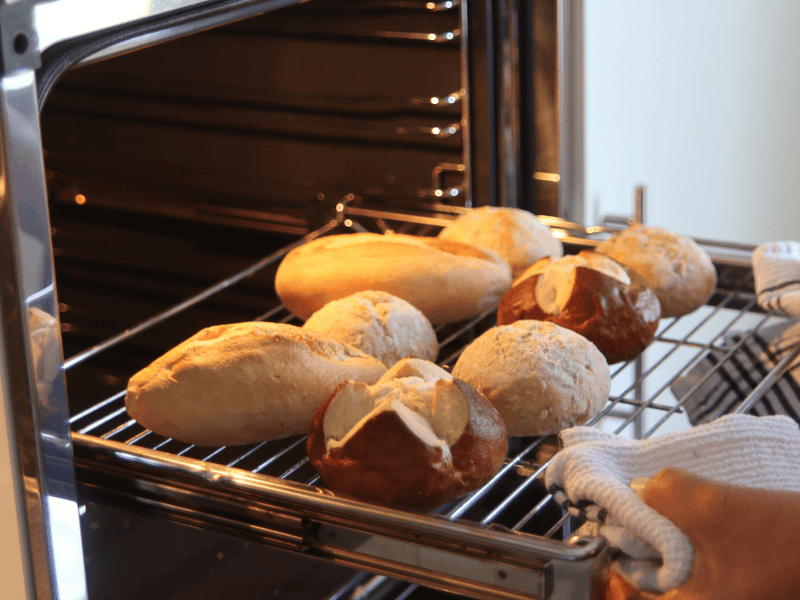 Person schiebt Ofengitter mit Brötchen darauf in den Backofen.