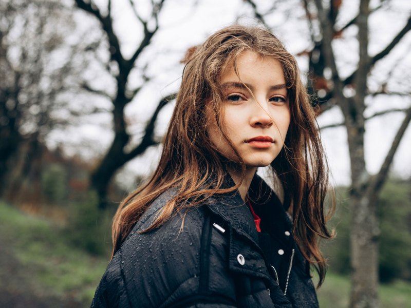 Porträt eines Mädchens von ca. 14 Jahren, das in einem herbstlichen Wald spazieren geht und ernst in die Kamera schaut.