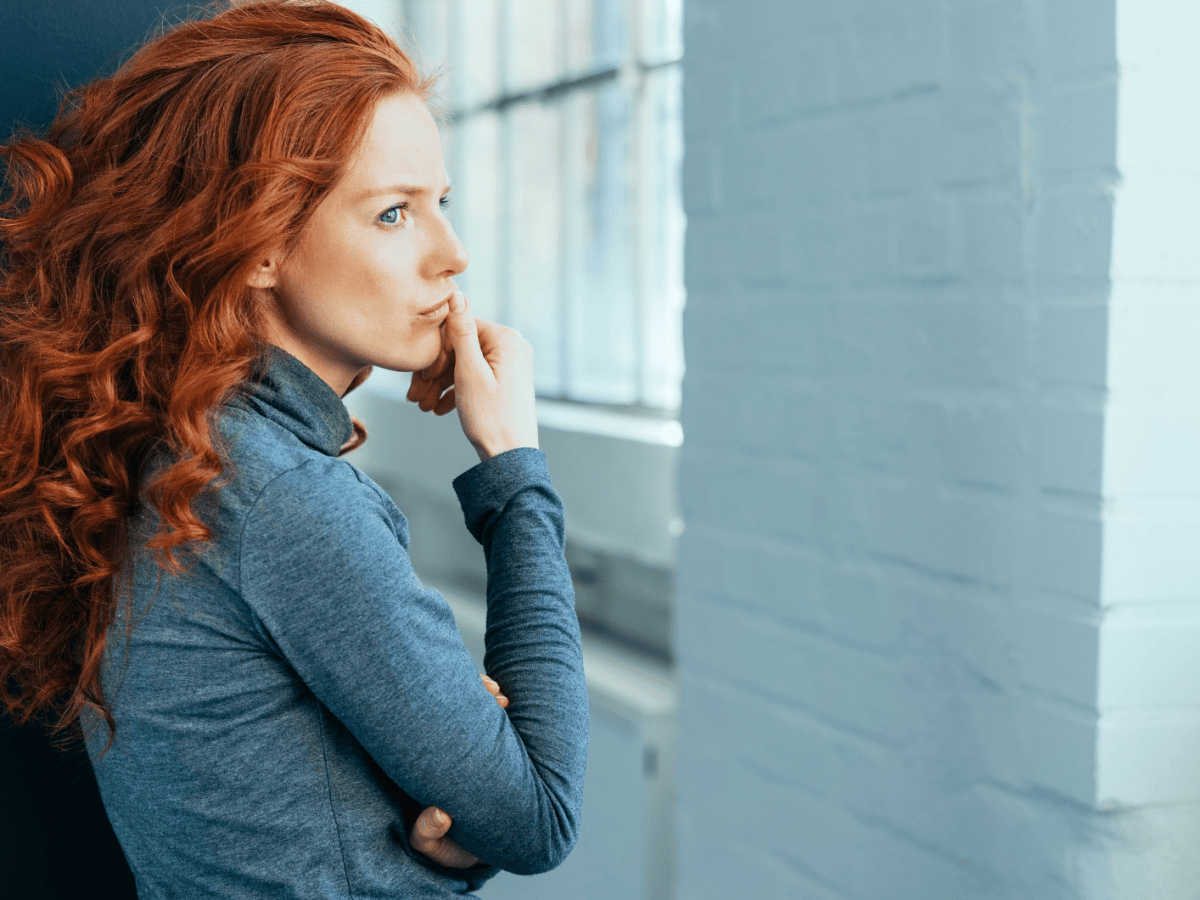Frau mit roten Haaren schaut nachdenklich nach vorne.