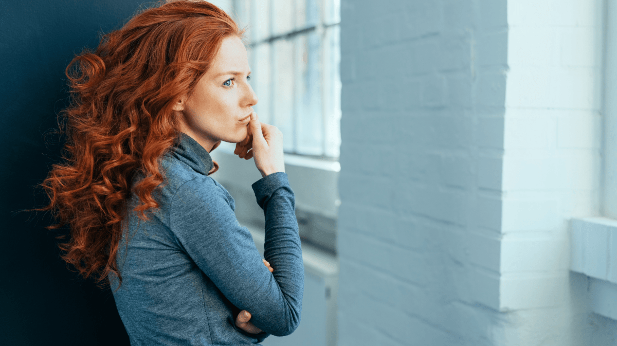Frau mit roten Haaren schaut nachdenklich nach vorne.
