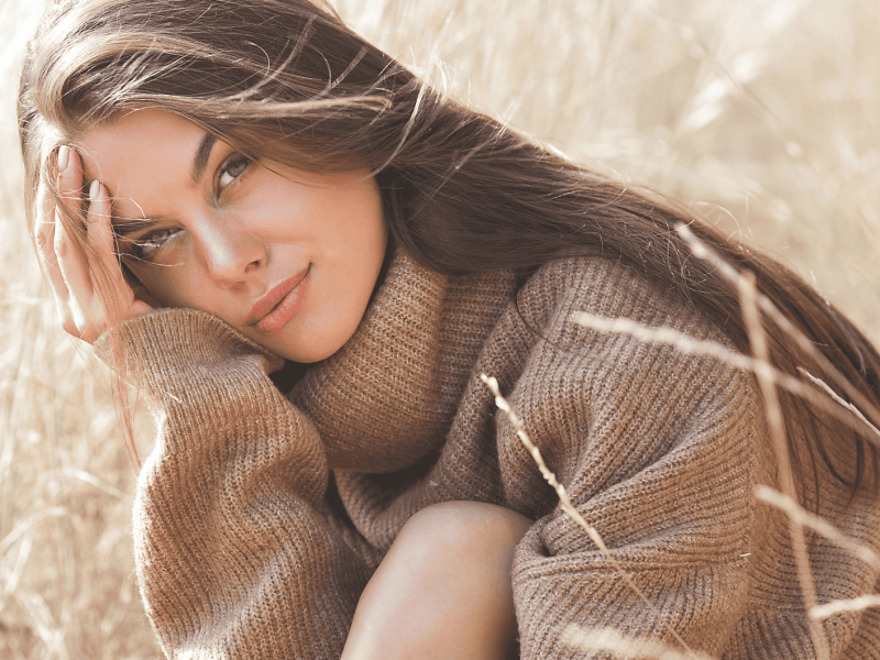 Junge Frau sitzt in Feld und schaut in Kamera.