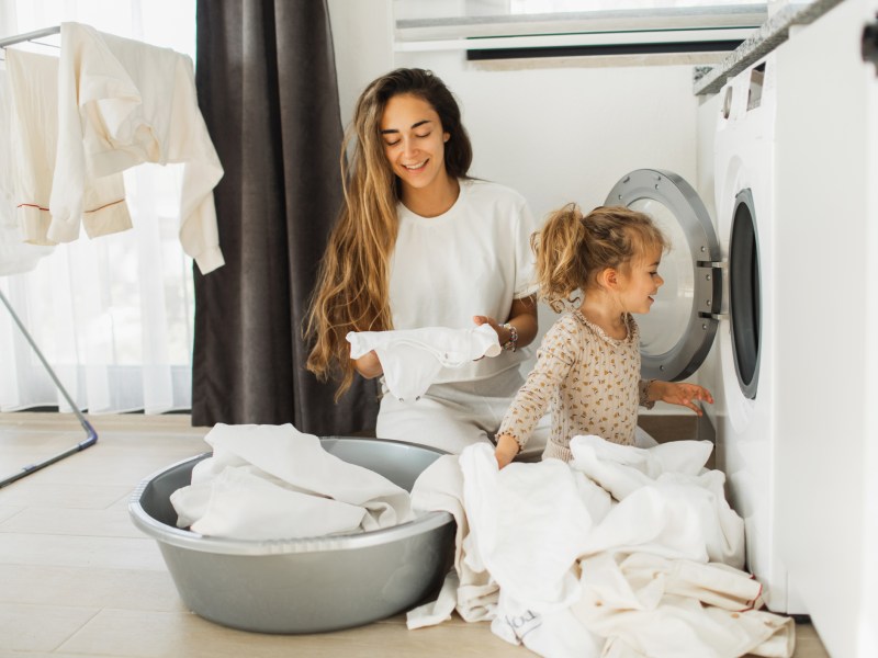 Mutter und Tochter vor Waschmaschine mit weißer Wäsche