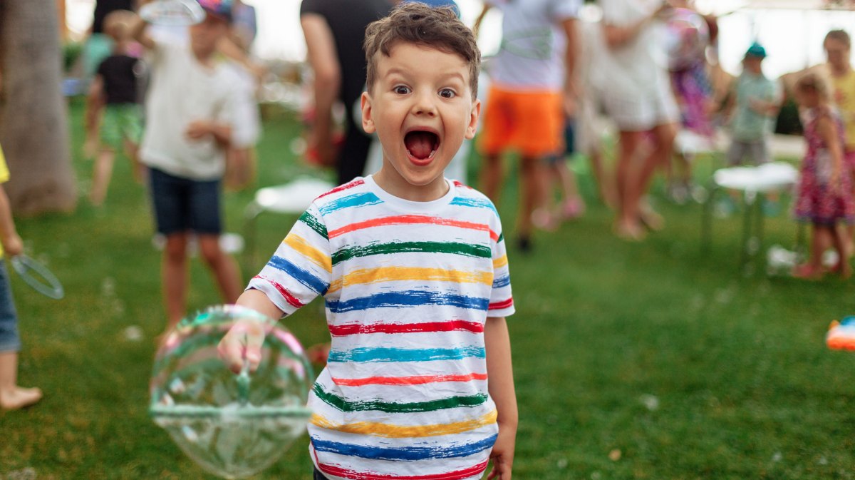 Junge, ca. 5 Jahre alt,an einem Sommerabend im Park, mit einer großen Seifenblase in der Hand.