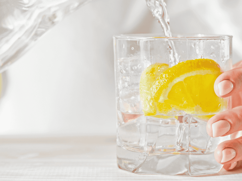 Frau gie&szlig;t Glas Wasser mit Zitrone ein.