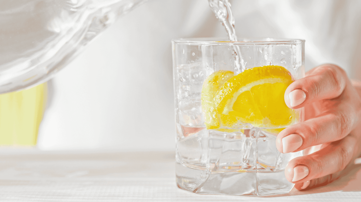 Frau gießt Glas Wasser mit Zitrone ein.