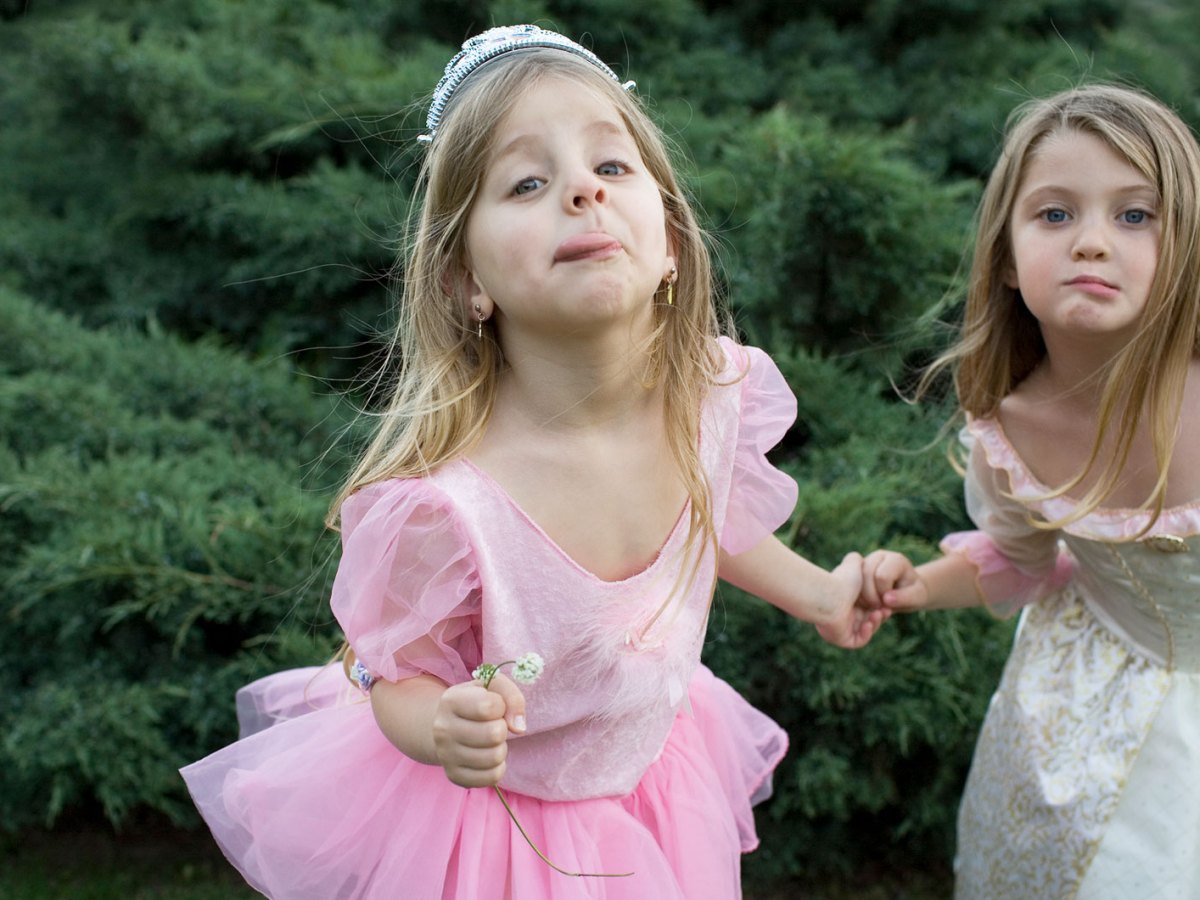 Zwei Mädchen, ca. 7 Jahre alt, stehen in Prinzessinnenkostümen im Garten und ziehen Grimassen Richtung Kamera.