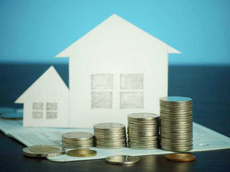 Gestapelte Münzen in aufsteigender Reihenfolge vor zwei weißen Papierhäusern auf einem Kontoauszug, symbolisieren Immobilienfinanzierung.