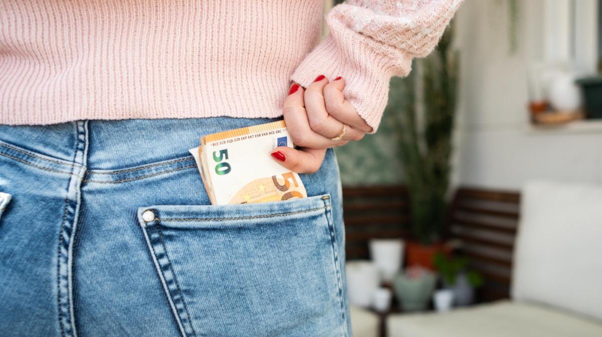 Frau holt Geldscheine aus ihrer Hosentasche hinten.