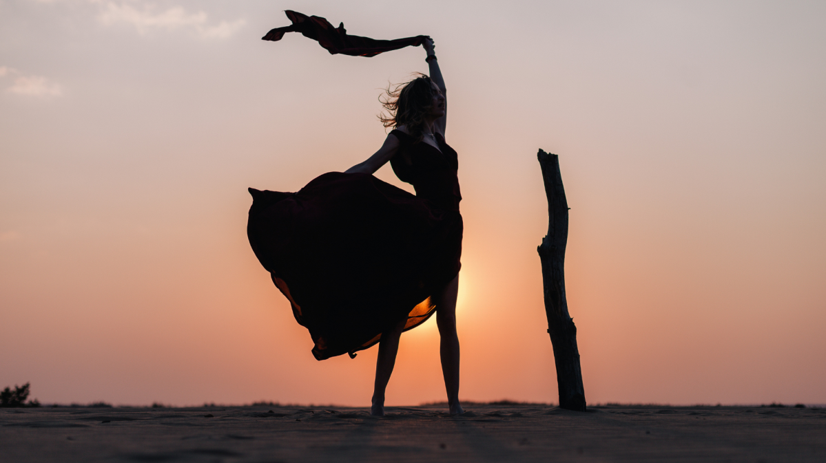 Frau steht vor dem Sonnenuntergang mit einem wehenden Rock