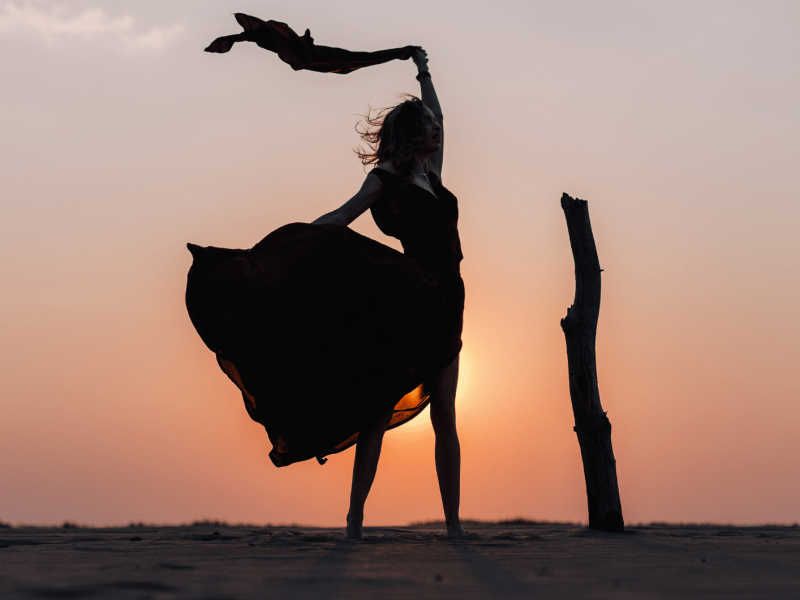 Frau steht vor dem Sonnenuntergang mit einem wehenden Rock