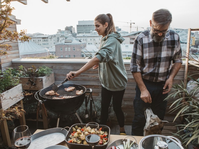 Mann und Frau grillen Würstchen auf dem Balkon.